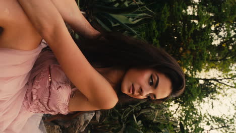 retrato de una joven morena caucásica jugando con su cabello en el jardín botánico con un vestido largo rosado, video vertical, cerrando los ojos