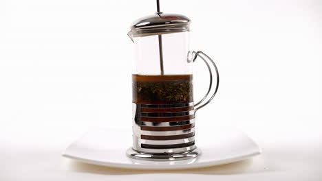 steeping loose-leaf tea in a french press on a white plate with a transparent design