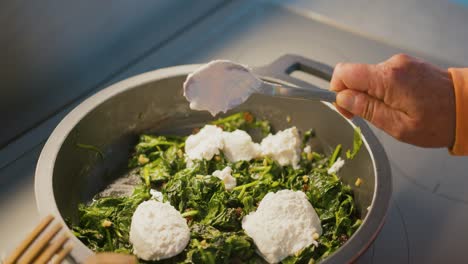 salpicando queso sobre las espinacas que se están cocinando en una sartén