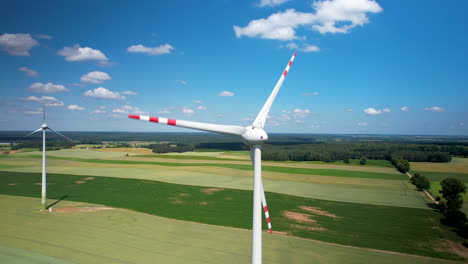 aerial wide shot of rotating wind turbine on agricultural grass field during sunny day - establishing drone shot - trucking shot