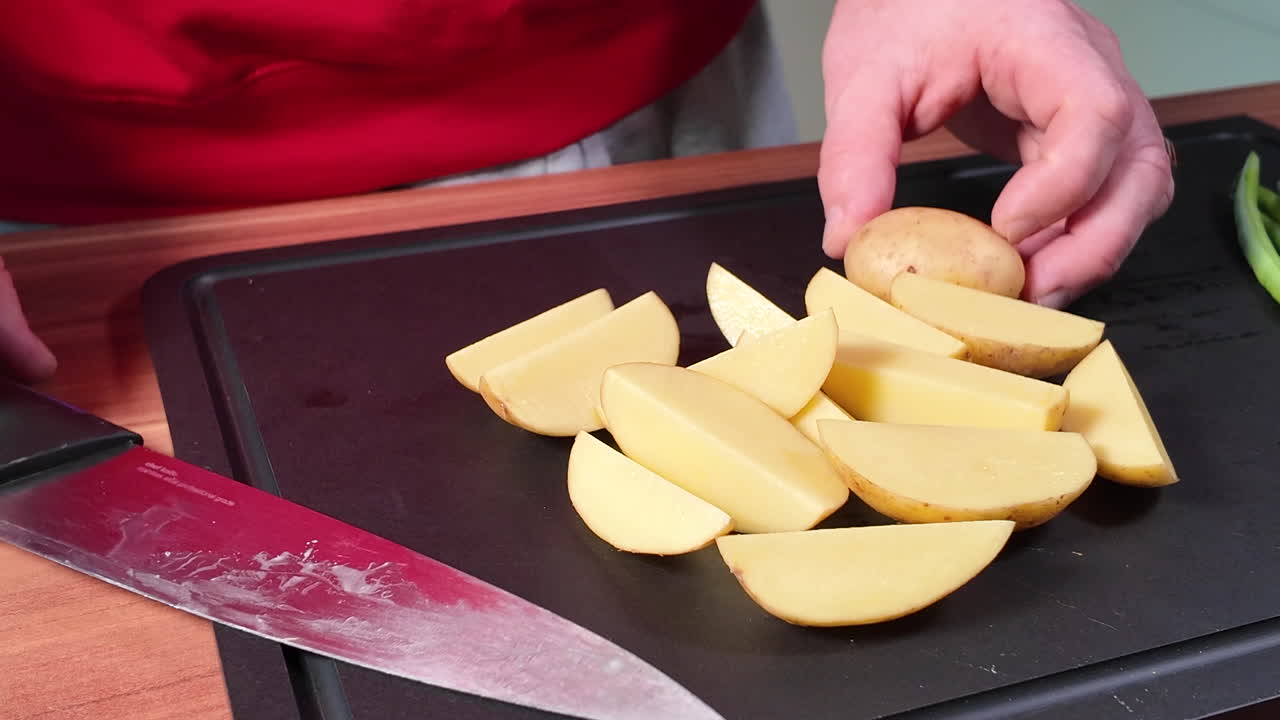 Primo piano di mani che tagliano una patata fresca a fette uniformi su un tagliere con un coltello da cucina affilato