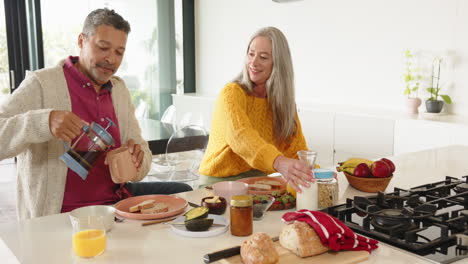 pouring coffee and milk, multiracial senior couple enjoying breakfast together at home kitchen table