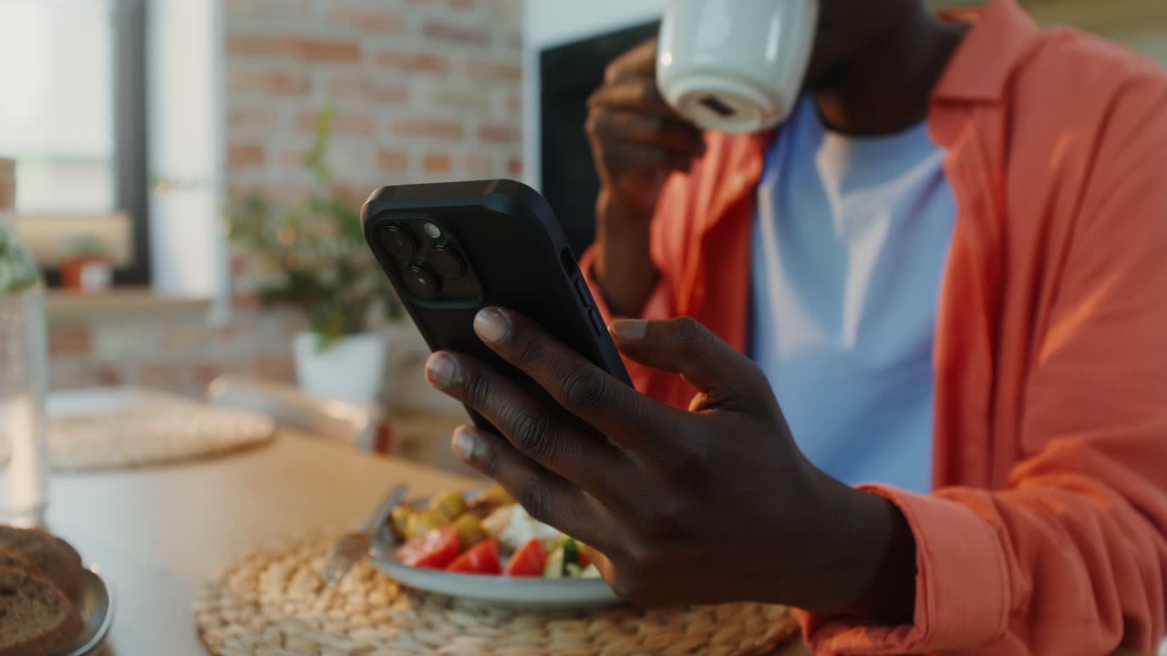 hombre comiendo almuerzo y usando teléfono inteligente en la cocina