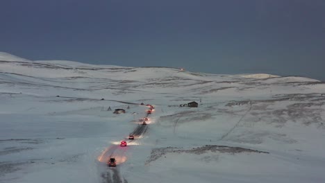 A-convoy-of-cars-driving-on-an-icy-road-towards-the-Nordkapp,-Norway-during-the-midwinter-solstice