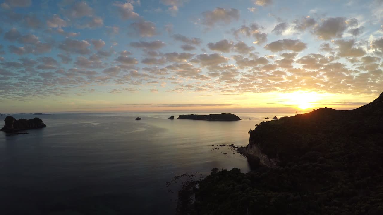 Sunset over calm waters with silhouettes of islands in the distance. Scenic coastal view from Lan Ha Bay, Vietnam. The vibrant sky reflects on the peaceful water creating a stunning scene