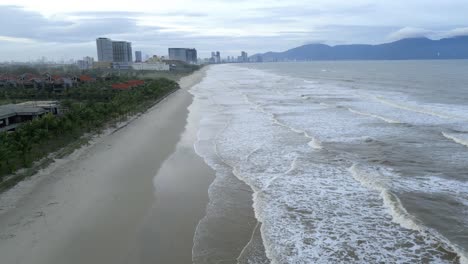 Hermosa-Toma-Aérea-De-Da-Nang,-Una-Playa-Bang,-Vietnam-Con-Las-Olas-Rodando-Hacia-La-Playa-Y-Rascacielos-En-El-Fondo