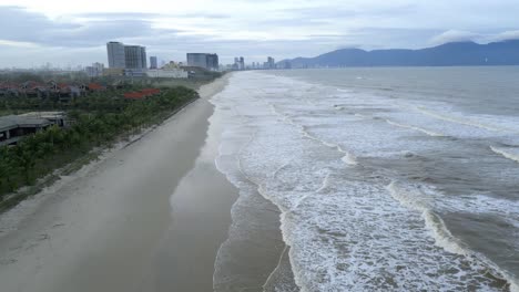 hermosa toma aérea de da nang, una playa bang, vietnam con las olas rodando hacia la playa y rascacielos en el fondo