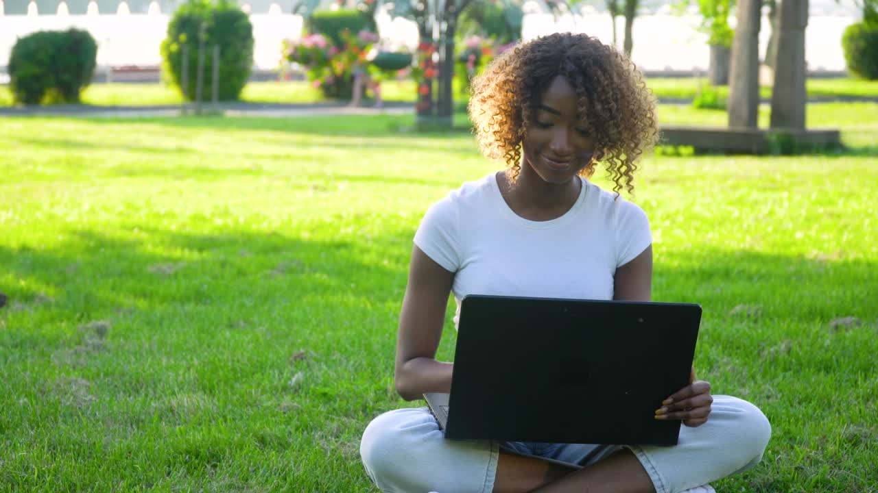 joven afroamericana usando una computadora portátil en el parque. una chica trabaja remotamente