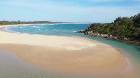 Drone-shot-of-the-South-Pacific-Ocean-and-Korogoro-Creek-with-wind-blowing-sand-across-a-sand-bar-at-Hat-Head-New-South-Wales,-Australia