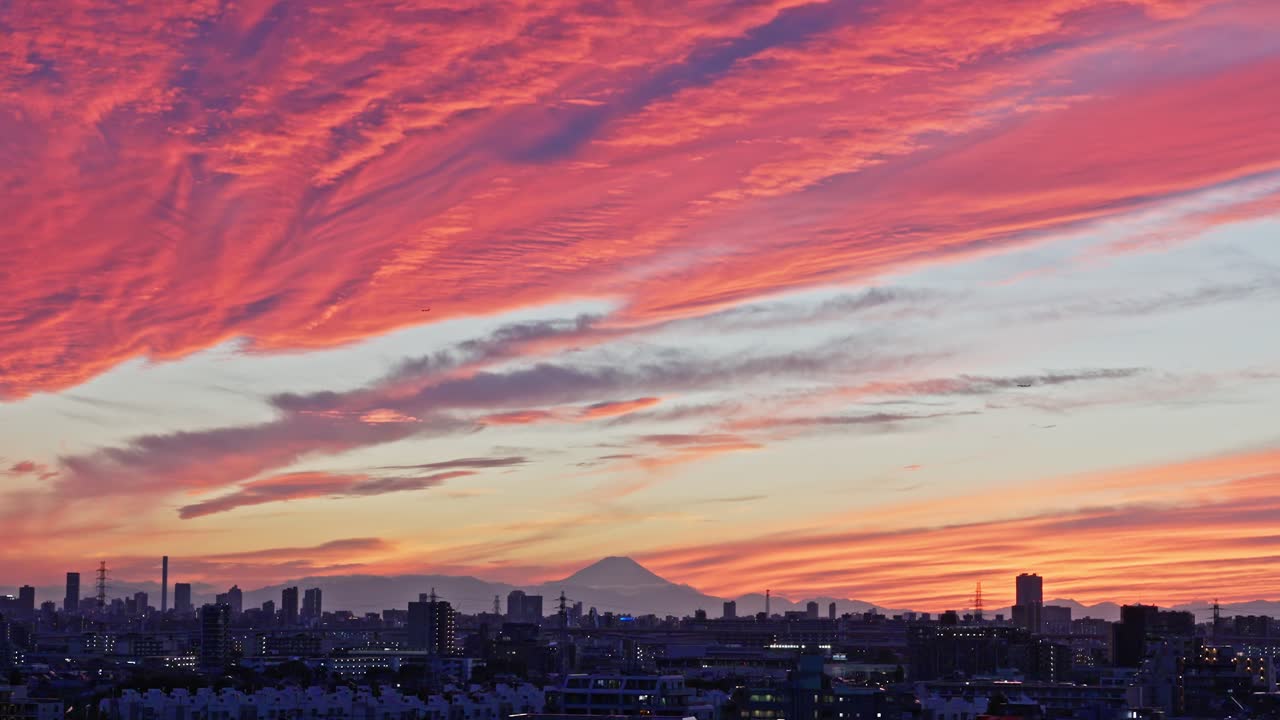 A spectacular, fiery sunset view with intense red and orange clouds above the city skyline and the silhouette of Mount Fuji