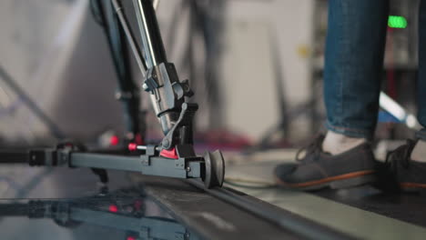 close-up shot of camera dolly system on track in professional studio. camera rig is in motion as technician adjusts gear. blurred background with studio lighting and colorful equipment visible