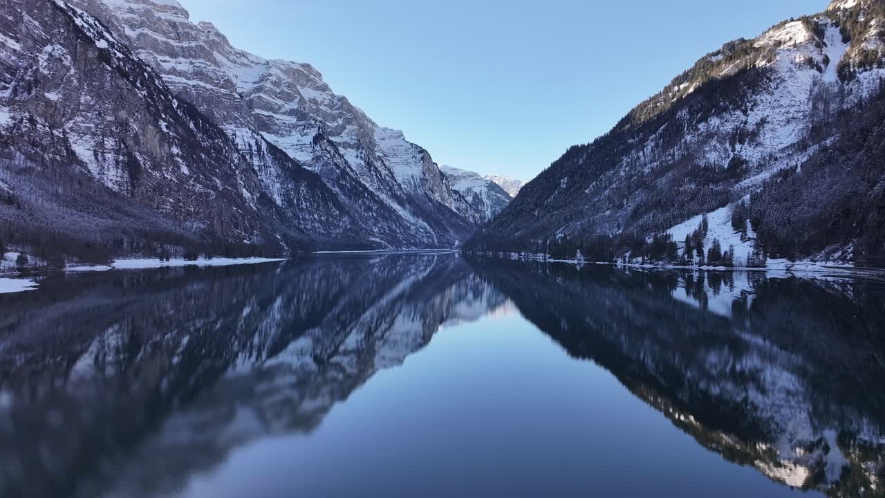 Aerial Klöntalersee reflecting snowy Alps in Klöntal, Switzerland, serene winter landscape