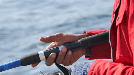 primer plano de la mano de un pescador sosteniendo una caña y un carrete