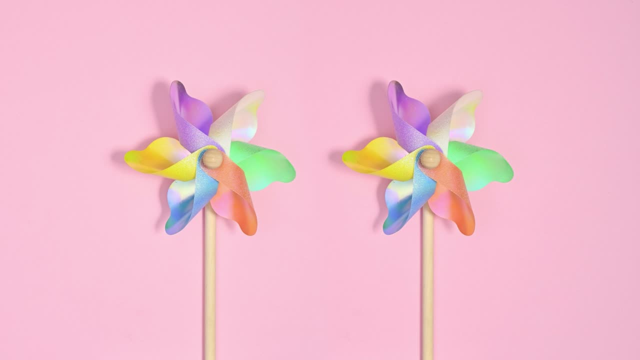 다채로운 플라스틱 풍차가 파스텔 분홍색 배경에 회전합니다.
