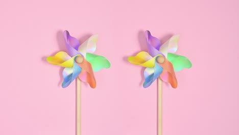 los molinos de viento de plástico coloridos giran sobre un fondo rosa pastel.