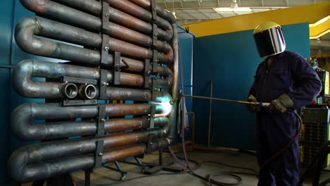 medium shot of a welder in full protective hse kit welding pipes at a factory with intense light and nice sparks from the welding operation