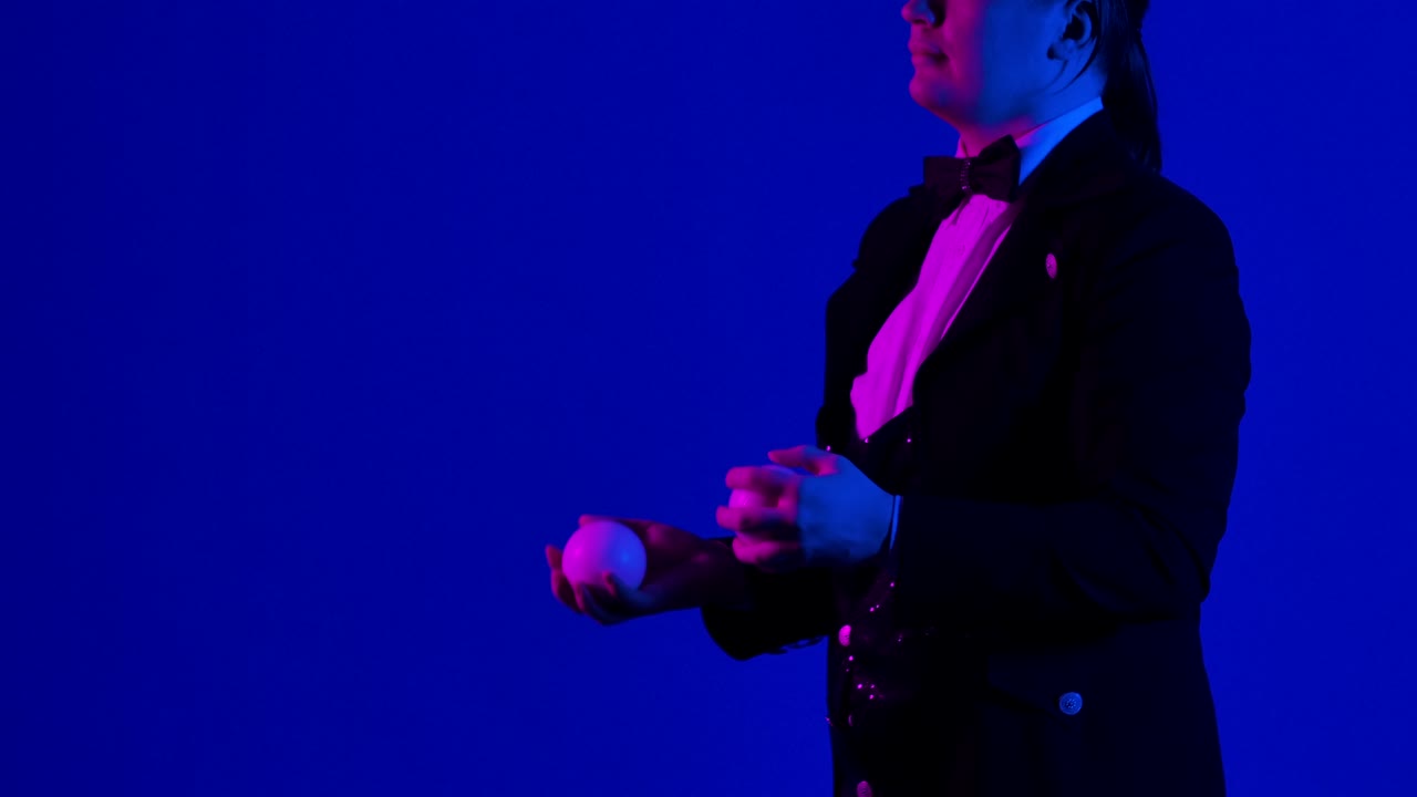 Side view man juggler shows tricks with white balls, tossing and catching them. Stylish showman practices concentration, dexterity and skill. Blue screen, chroma key. Close up. Slow motion