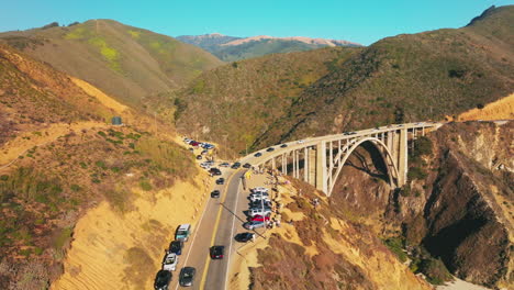 cars moving slowly to and from the bridge in the mountains. california rocks at the coast of pacific on sunny daytime. aerial view.