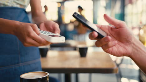 Primer-Plano-De-Un-Hombre-En-Una-Cafetería-Pagando-La-Factura-Con-El-Pago-Por-Teléfono-Móvil-Sin-Contacto