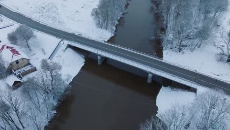 Puente-Del-Río-Abava-Cerca-Del-Pueblo-De-Renda,-Paisaje-Cubierto-De-Nieve,-Vista-Aérea,-Toma-En-órbita-De-Ojo-De-Pájaro