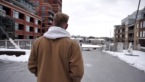 slo mo walk and pan around a blonde young man with brown a brown jacket on millennium bridge in denver colorado on cold snowy day