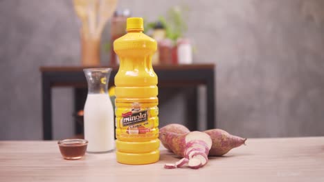 a woman grabbing a bottle of lauric oil with white vinegar, fish sauce and sweet potatoes prepared on the table - close up shot