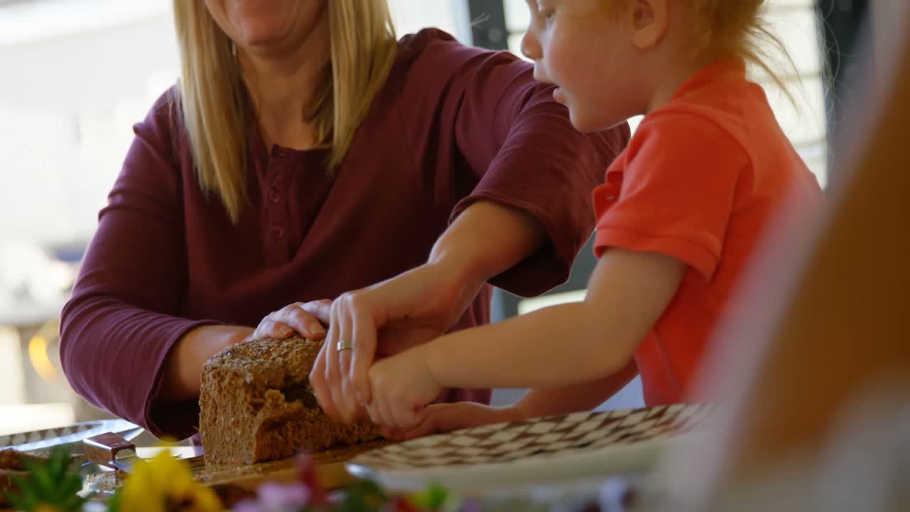 Mother and son cutting loaf of bread on dining table 4k