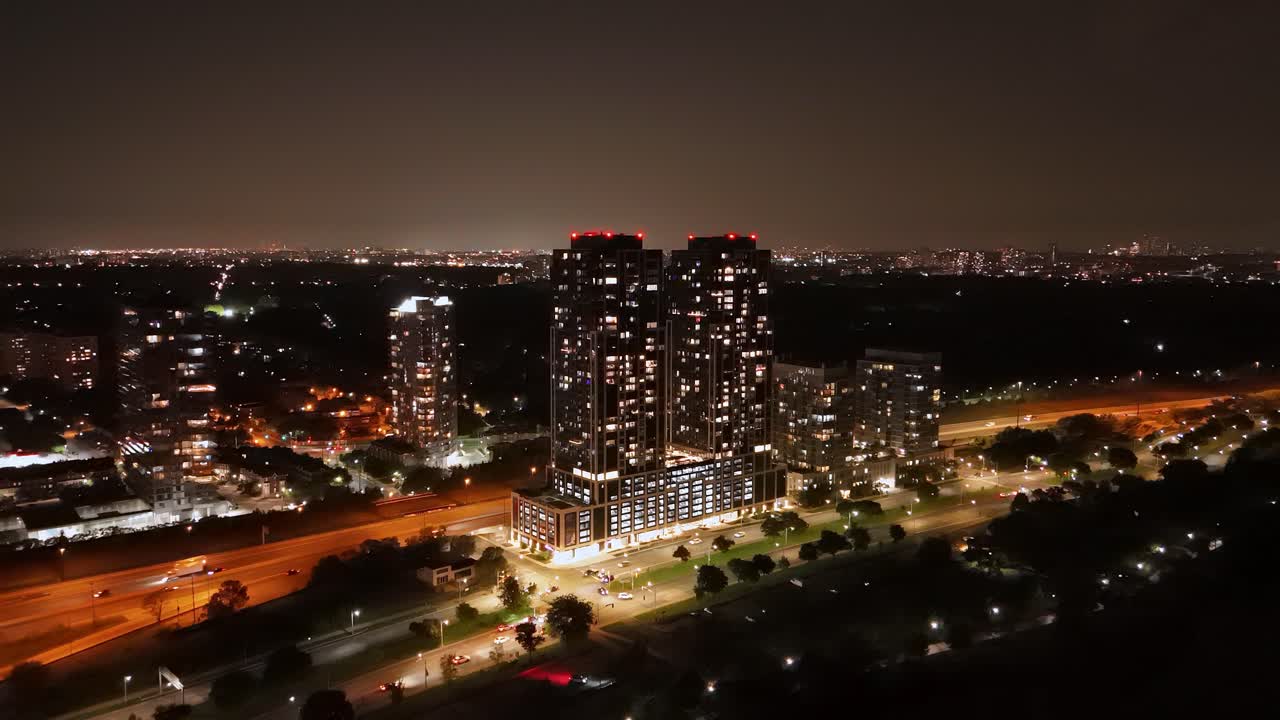 Nighttime aerial view of Parklawn’s condo towers overlooking Lake Ontario, with glowing city lights and highway traffic leading toward downtown Toronto’s skyline
