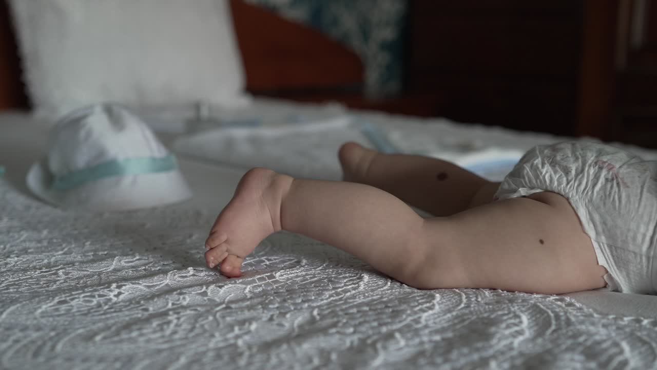 Baby in diaper lying on white lace bedspread with white sun hat in soft natural light
