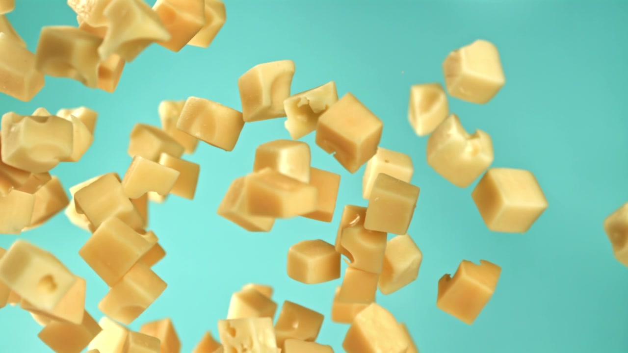 Dés de fromage tombant au ralenti sur un fond turquoise