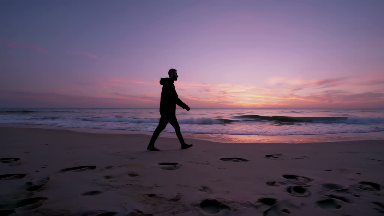 Person Silhouetted Against a Vibrant Sunset Sky Walking on the Beach