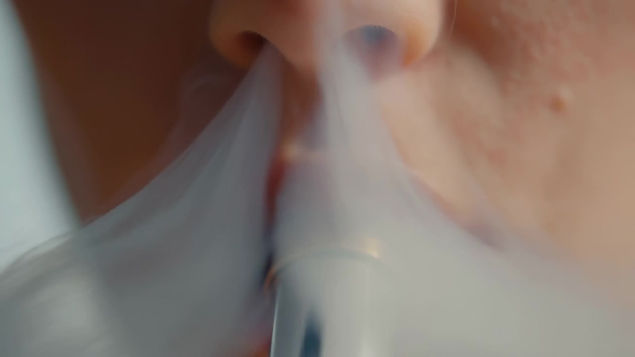 Una vista estremamente ravvicinata mostra labbra attorno a un vape cilindrico lucido mentre un denso vapore fuoriesce da entrambe le narici, diffondendosi gradualmente sul viso inferiore in una luce calda e soffusa.