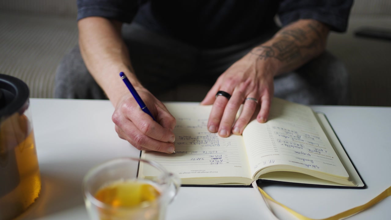 Person writing productivity book at desk, close-up view