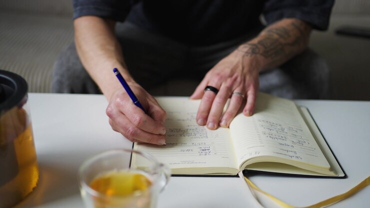 Person writing productivity book at desk, close-up view