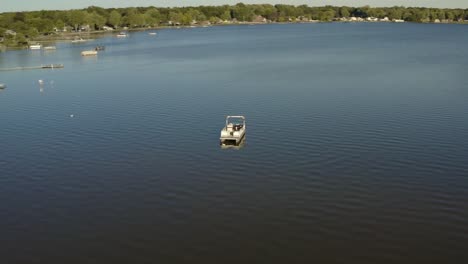 Orbiting-drone-shot-of-a-boat-on-a-blue-lake-overseeing-trees-and-houses