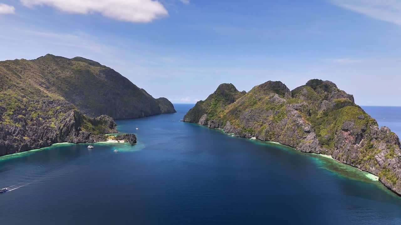 Aerial view of Star Beach on Tapiutan Island in the Philippines with deep blue waters, cliffs, and boats anchored near coral reefs along the lush coastline under clear blue skies
