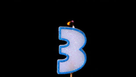 Three-birthday-candle-flickering-and-extinguishing-on-black-background