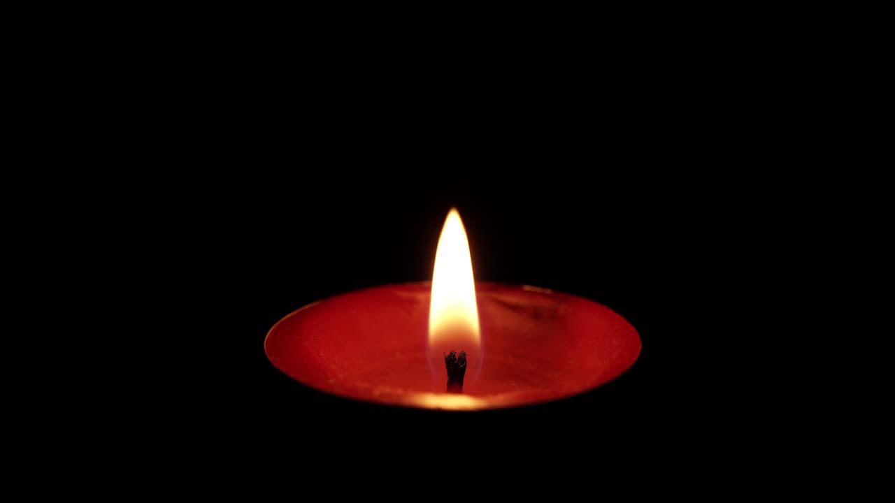 Fiamma di candela galleggiante che si accende su sfondo nero, condizioni ventose che la spengono, scatto macro.