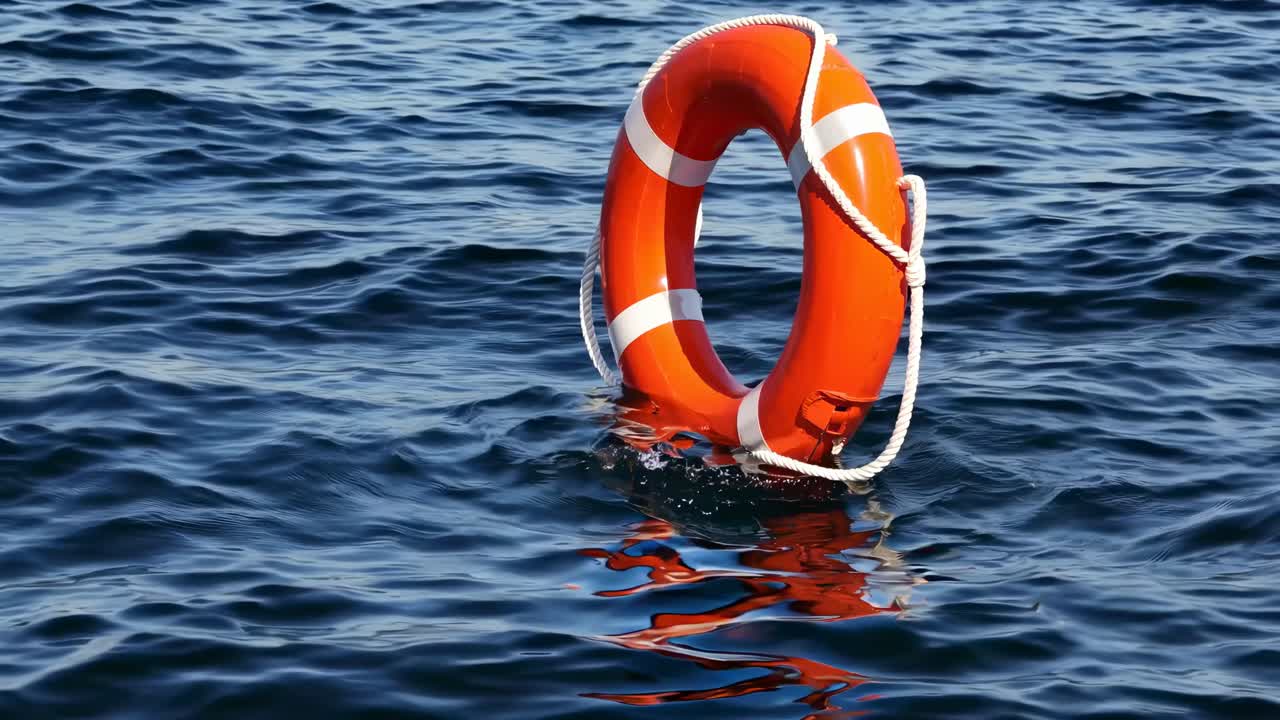 A vibrant orange lifebuoy floating on rippling blue water, captured from a low angle