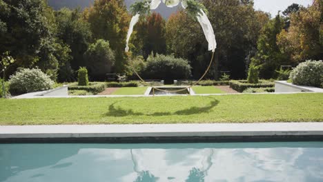 wedding arch with decorations in sunny summer garden with swimming pool, in slow motion