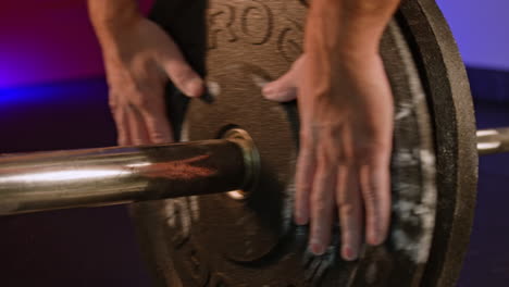 muscular male bodybuilder stringing round black weights onto barbell