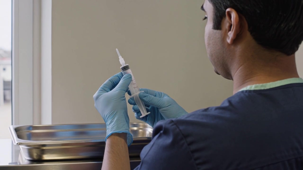 Placing tray, nurse preparing syringe at window cart for procedure, in navy scrubs, blue gloves