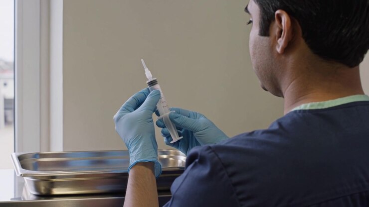 Placing tray, nurse preparing syringe at window cart for procedure, in navy scrubs, blue gloves
