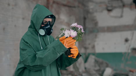 nature in danger. ecologist in safety suit and gas mask holding broken flowers in abandoned place. biochemical attack. polluted environment.