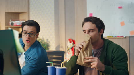 happy man proposing sandwich colleague at office closeup. two guys eating lunch