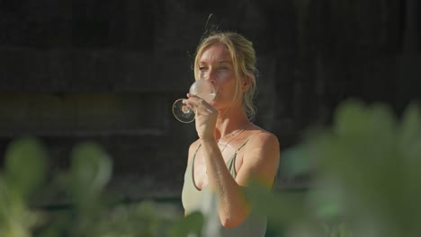 elegant woman taking sip from champagne with golden hour sunlight on face