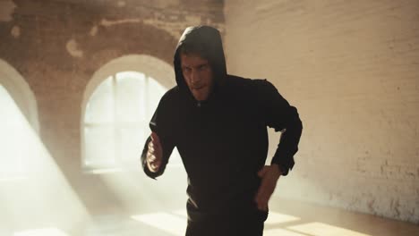 a man in a hooded sportswear runs in place for endurance in a sunny gym. sports activities to improve stamina