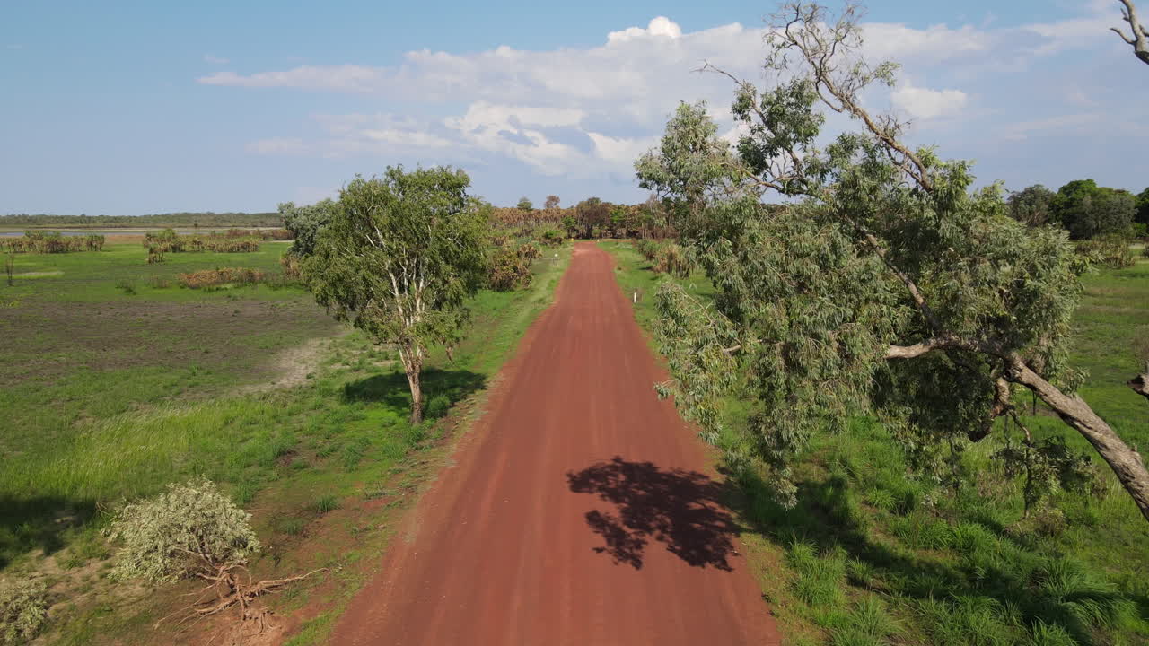 toma de drones en movimiento bajo de una larga carretera roja recta y matorrales verdes cerca del parque natural de la jungla de holmes, darwin, territorio del norte