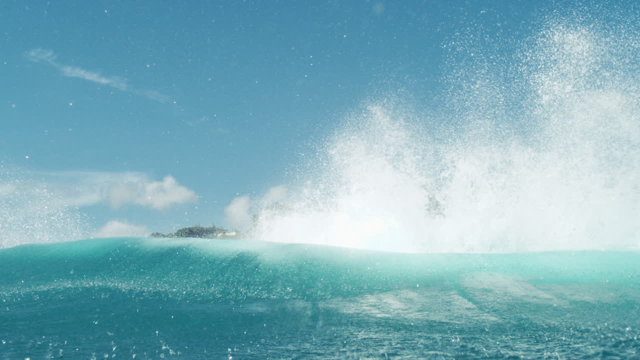 Turquoise wave breaks under sunny sky with fine mist and sparkling highlights