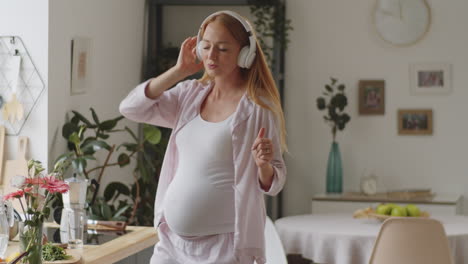 mujer embarazada bailando a la música en la cocina